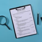 Flat lay magnifying glass and resumes applicants on blue background. Job search concept.